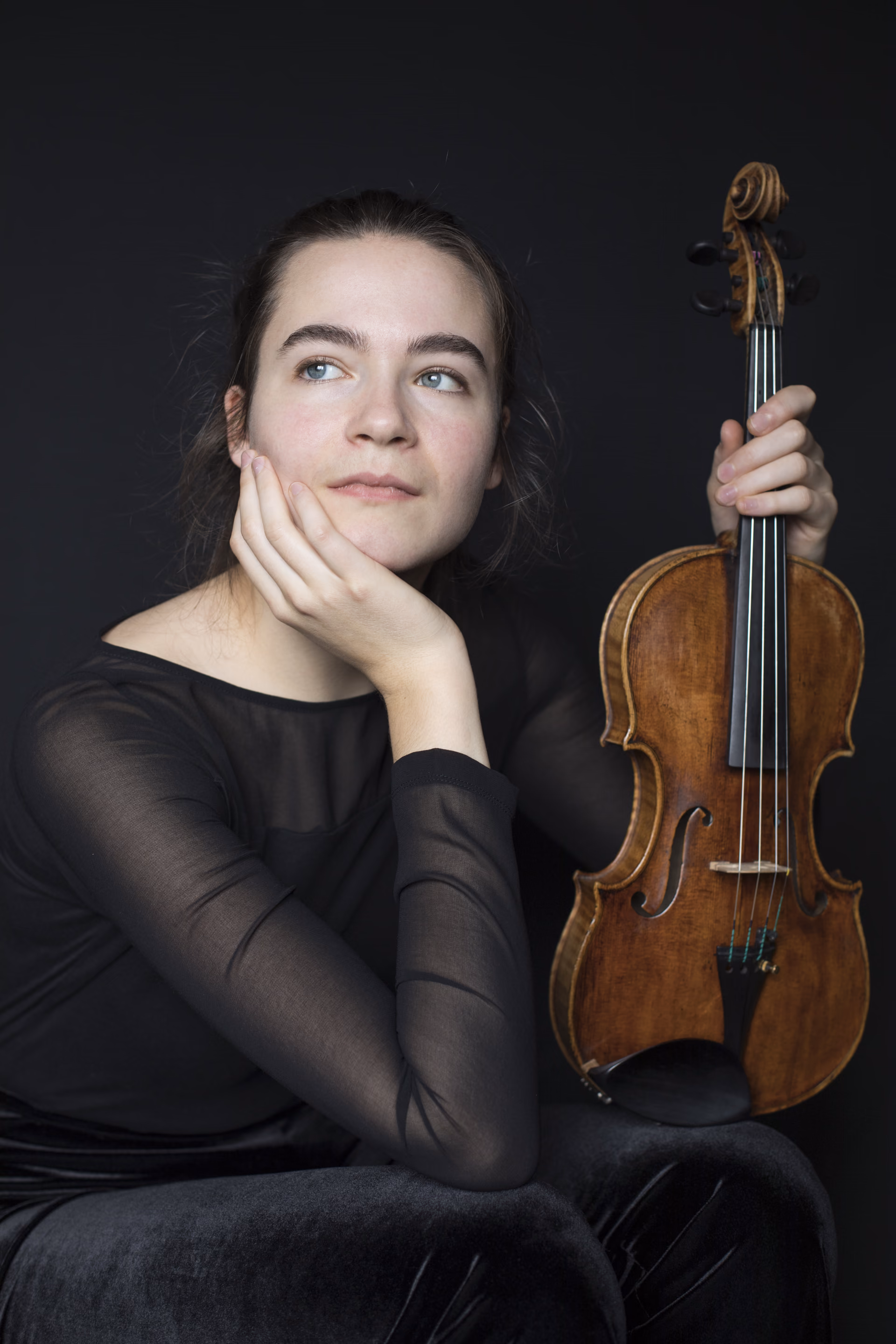 Hadewych with violin, leaning her head on her hand, looking away