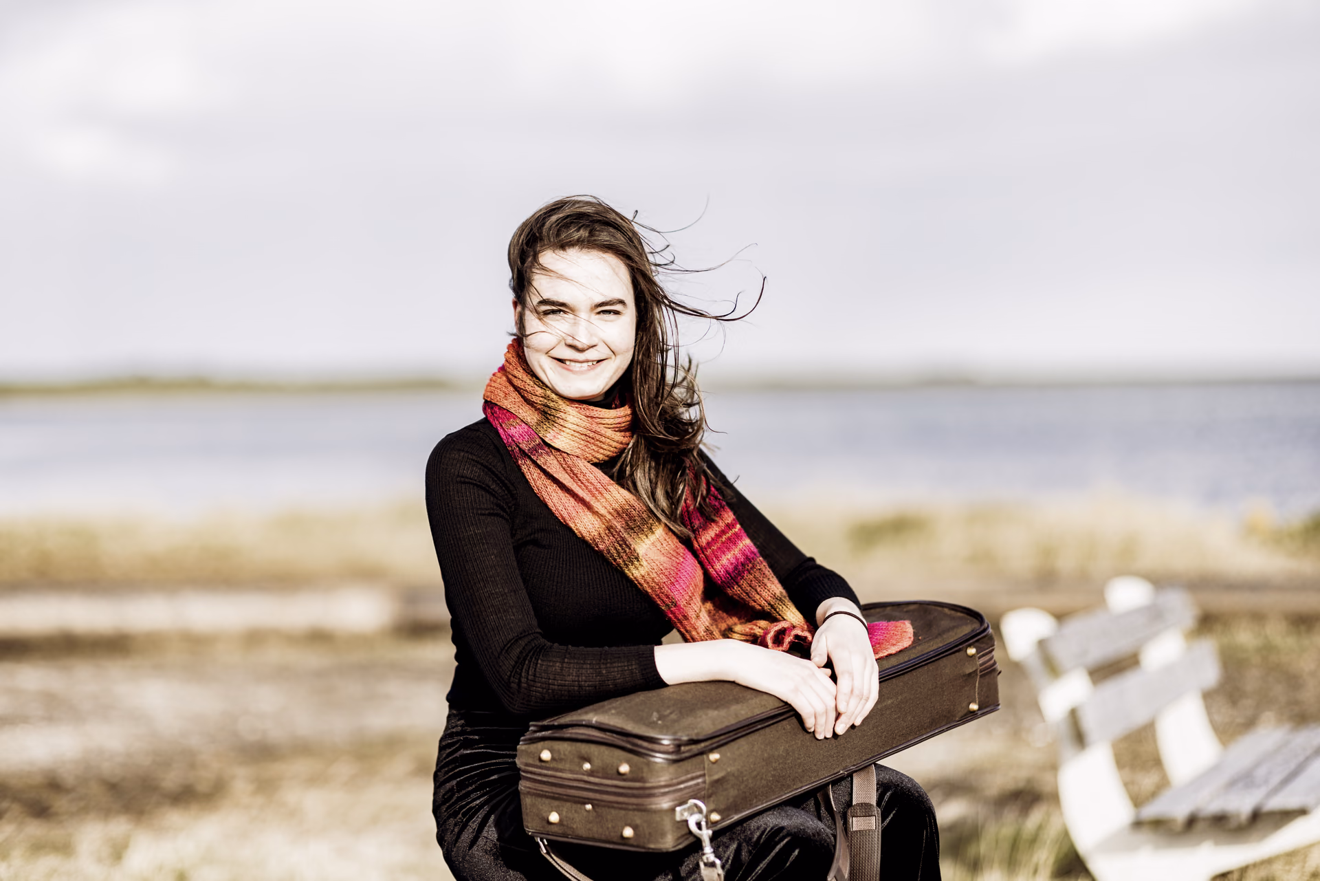 Hadewych outside with colorful scarf holding violin case, looking into the camera