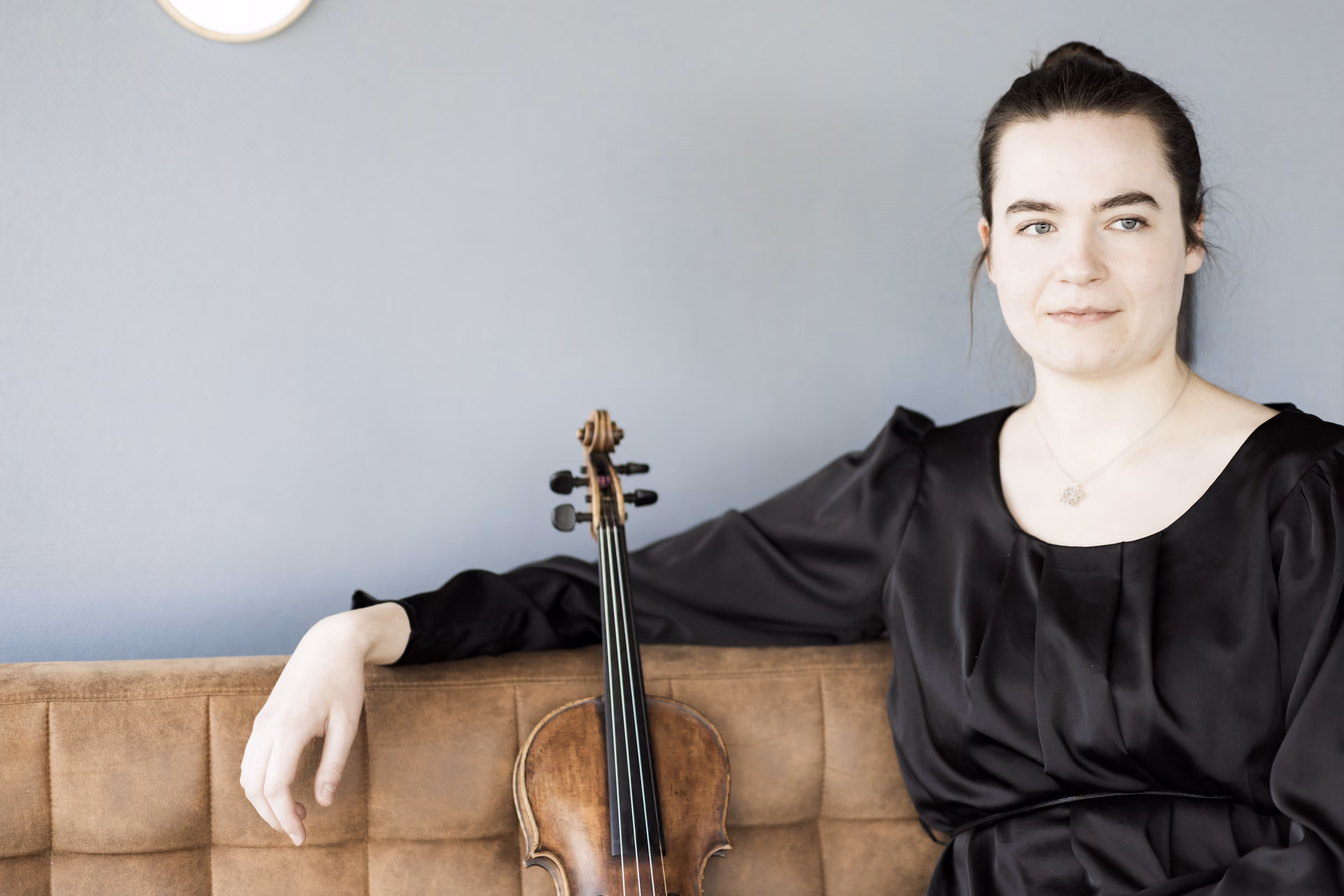 Hadewych sitting next to violin against blue wall looking away
